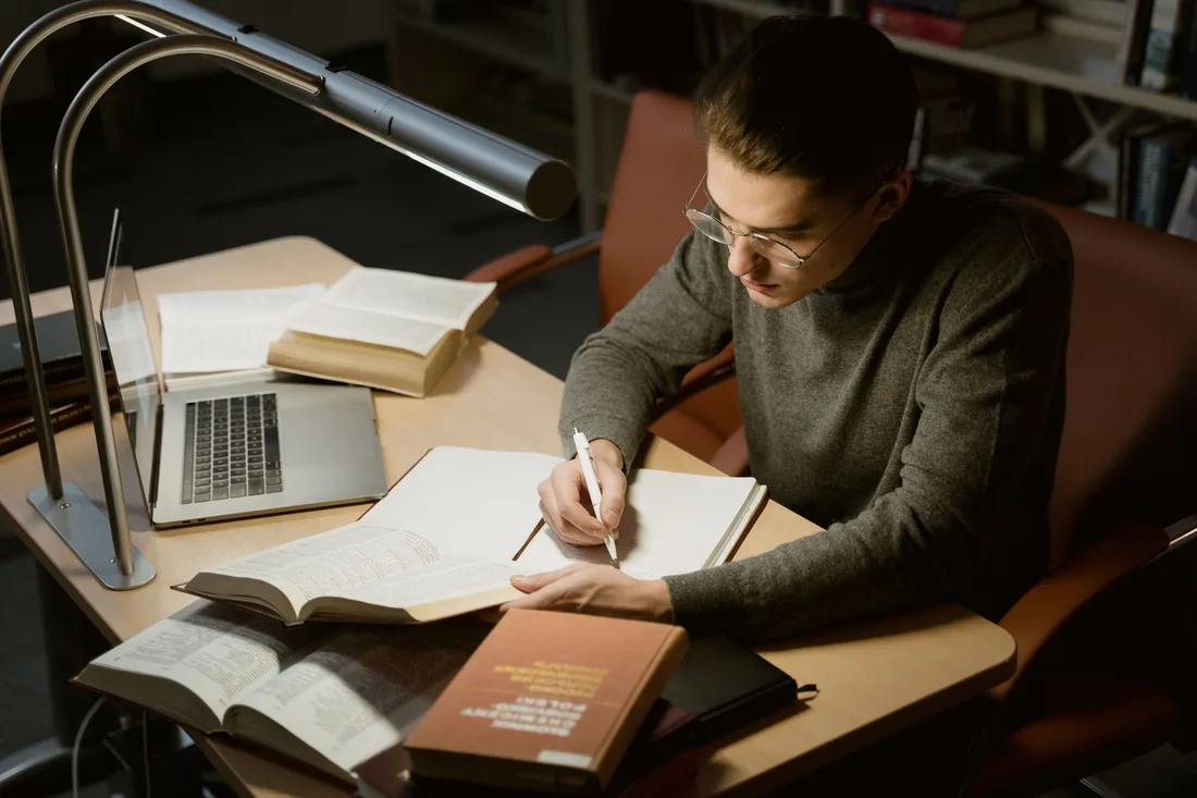 Personne révisant à un bureau avec livres, ordinateur portable et lampe