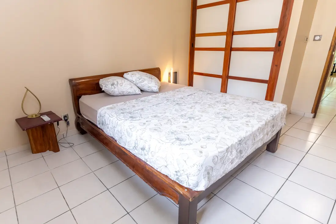 Chambre du T2 Mahury à Rémire-Montjoly : lit double en bois devant des panneaux coulissants d’inspiration japonaise