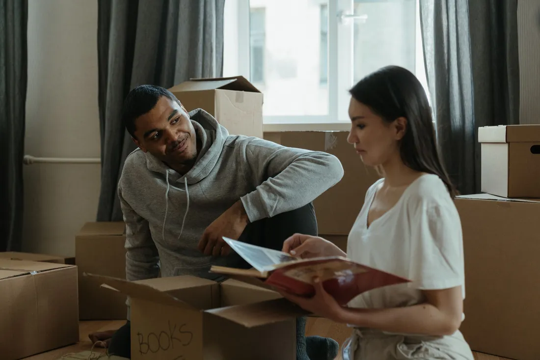 Jeune couple installant ses cartons de déménagement dans le salon d'un appartement, à la recherche de livres, pendant une installation temporaire