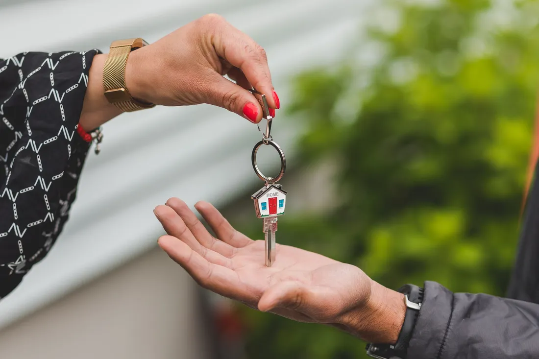Remise d'une clé de maison, avec porte-clés en forme de maison marqué HOME, d'une main à l'autre : entrée dans un logement