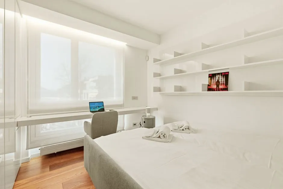 Chambre d'un appartement meublé avec bureau, ordinateur portable et linge de maison préparé pour l'accueil d'un collaborateur en mission