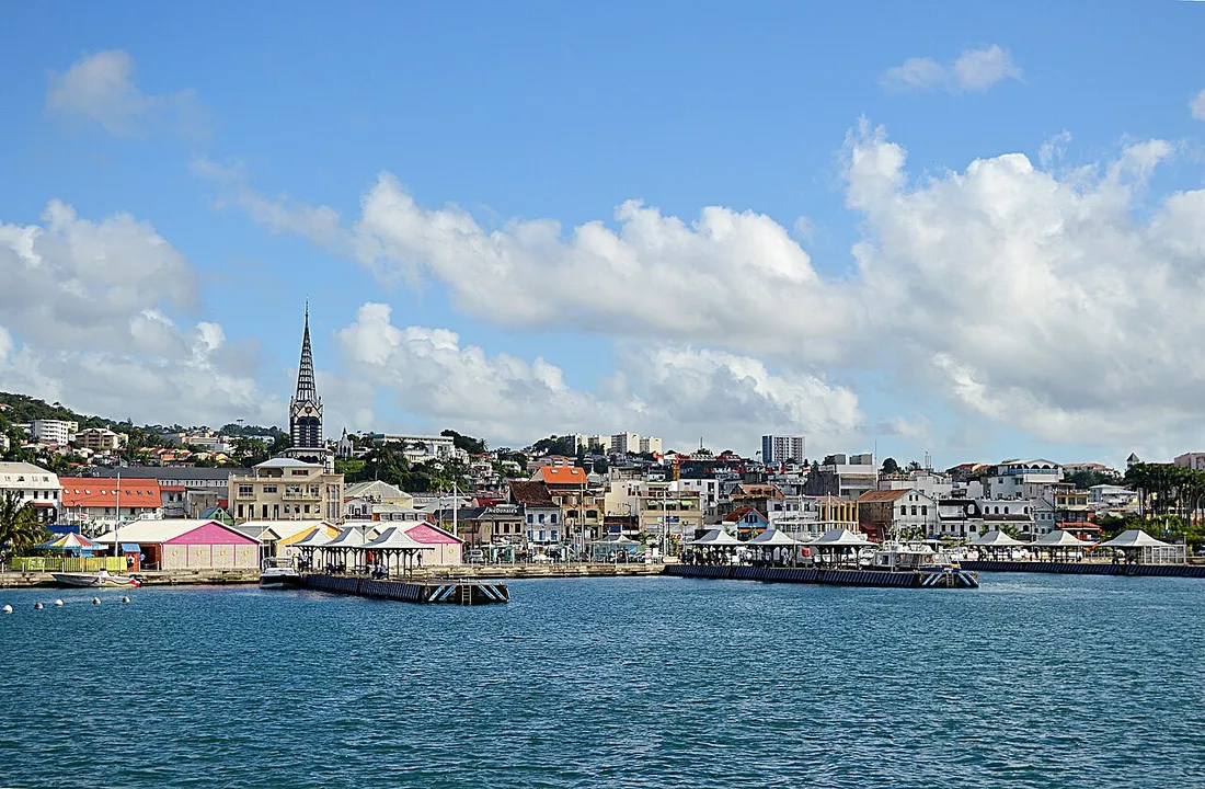 Front de mer de Fort-de-France en Martinique vu depuis la baie, avec les pontons, les carbets colorés et la flèche de la cathédrale Saint-Louis dominant les immeubles du centre-ville