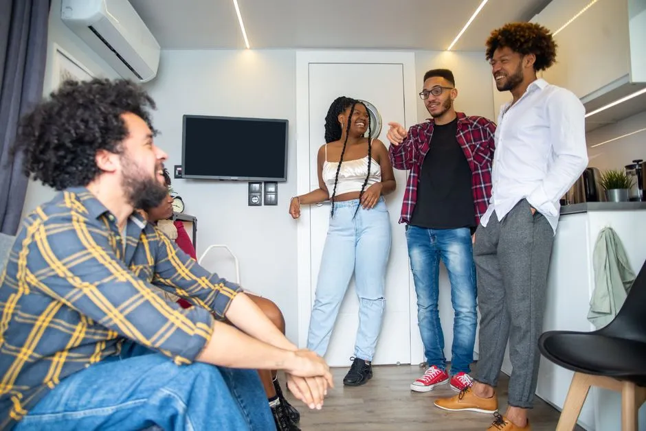 Groupe de six adultes réunis et souriants dans le séjour d'un appartement moderne équipé d'une cuisine ouverte et de la climatisation