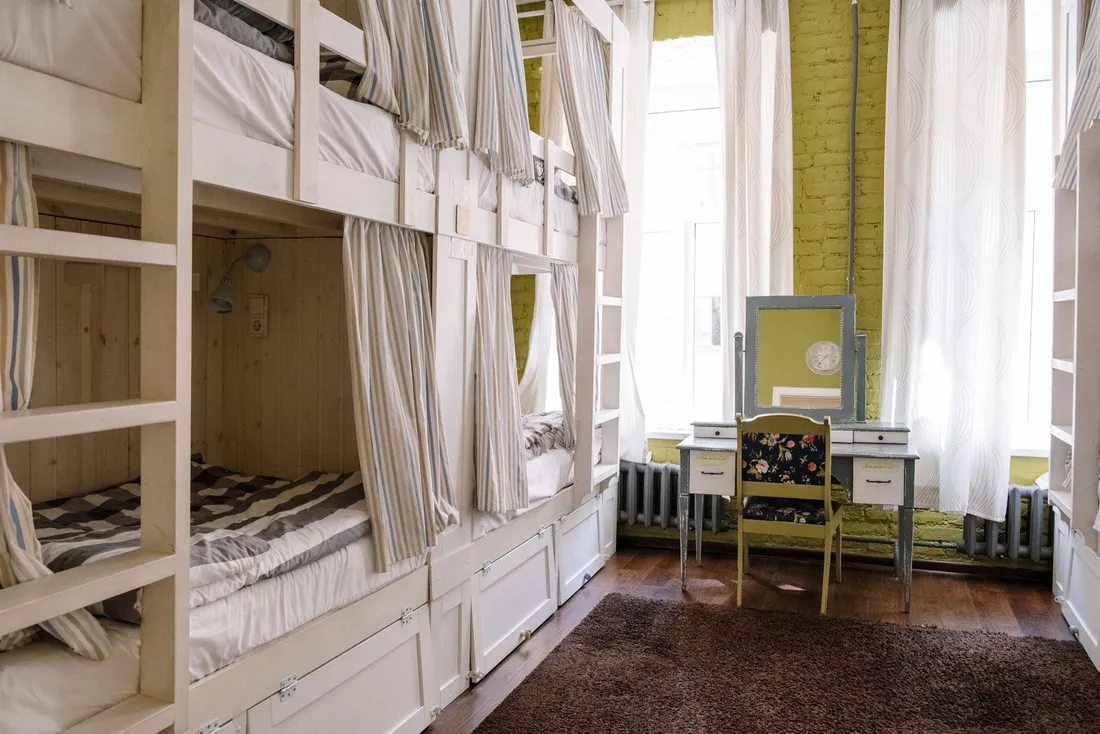 Chambre partagée d'auberge avec lits superposés en bois et rideaux d'intimité, solution économique pour héberger plusieurs collaborateurs