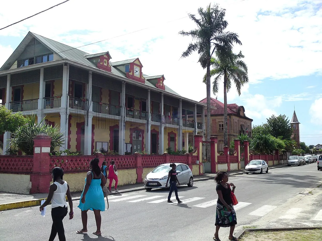Rue du centre de Saint-Laurent-du-Maroni, dans l'ouest guyanais, avec ses bâtiments coloniaux à galeries et des passants traversant la chaussée
