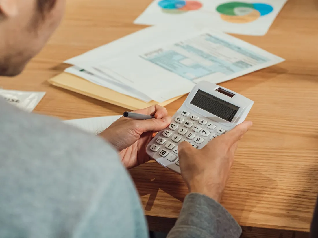 Personne assise a un bureau qui utilise une calculatrice, un stylo a la main, au-dessus de documents et d'une facture