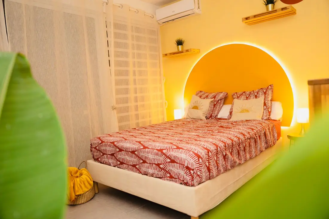 Chambre au Cocon Chic : tête de lit en arche jaune rétroéclairée, parure terracotta et voilages clairs