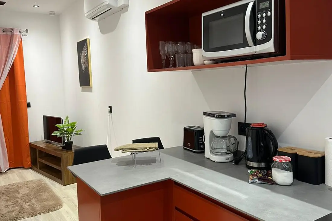 Coin cuisine rouge d’un logement de la Résidence Francis : micro-ondes en hauteur, cafetière, bouilloire et grille-pain sur le plan gris