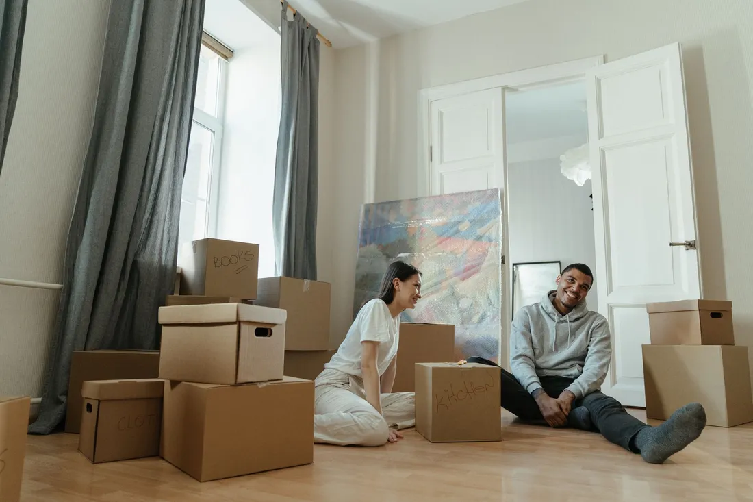 Jeune couple souriant installe au milieu de cartons de demenagement dans leur nouvel appartement
