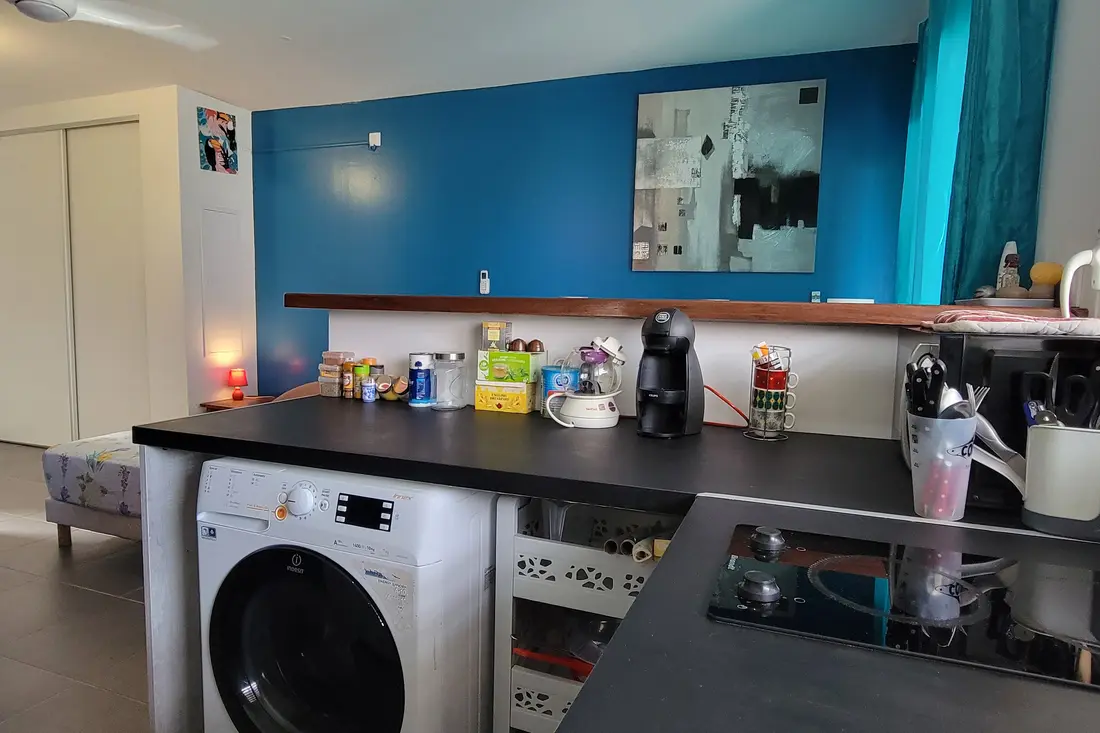 Kitchen corner at Sweet Dreams: black worktop, washing machine under the bar, coffee machine and utensils, blue wall behind