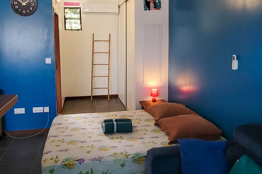 Studio at Sweet Dreams: blue walls, bed with folded towels, air conditioning and a bamboo ladder by the entrance
