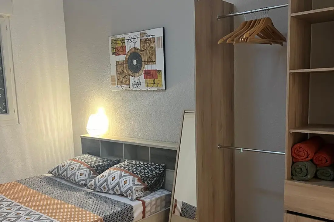 Chambre d’un appartement Cayenne Chic : lit aux motifs graphiques, penderie ouverte avec cintres en bois et serviettes roulées