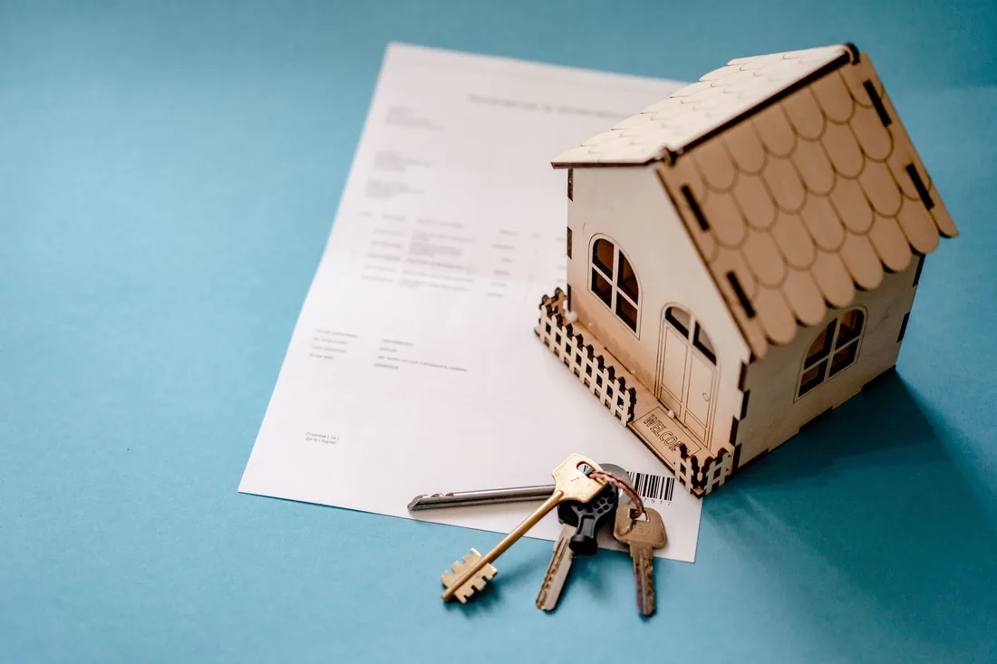Maison miniature en bois posée à côté de clés et d'un contrat