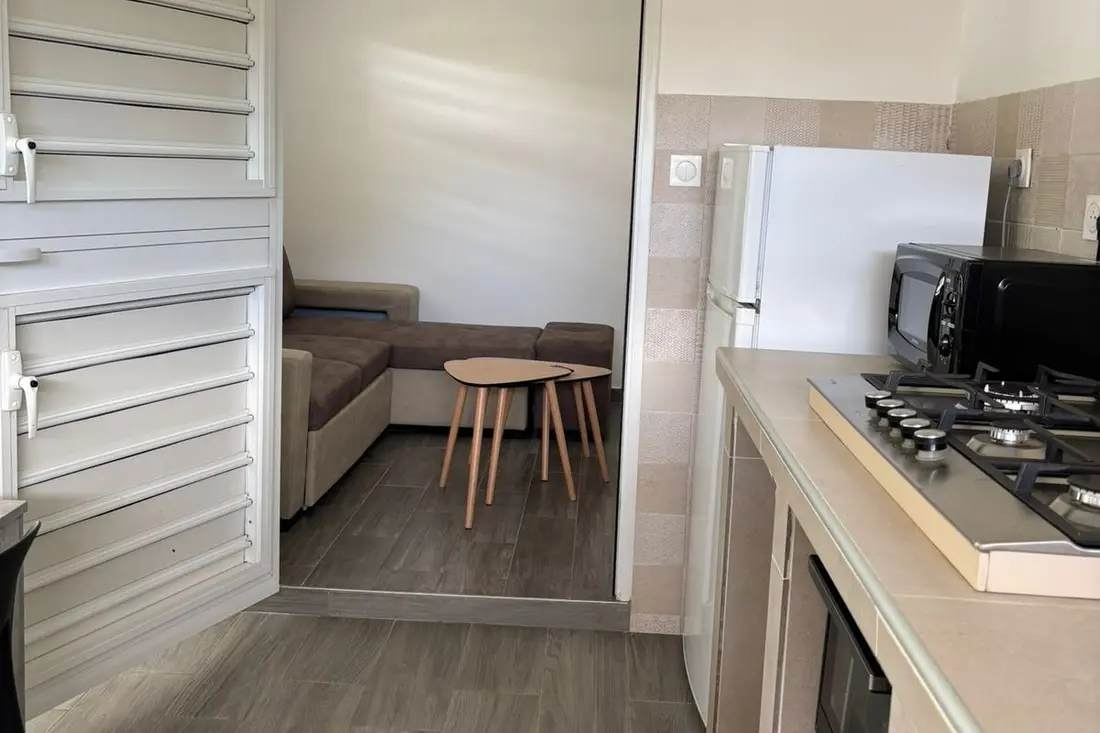 Vue de la cuisine de la Tropikana vers le salon : plaques gaz au premier plan, canapé d’angle et tables gigognes au fond