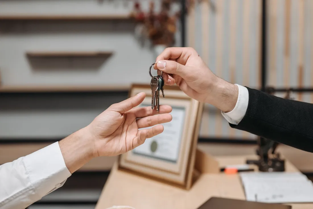Un professionnel en costume remet les clés d'un logement à un locataire au-dessus d'un bureau