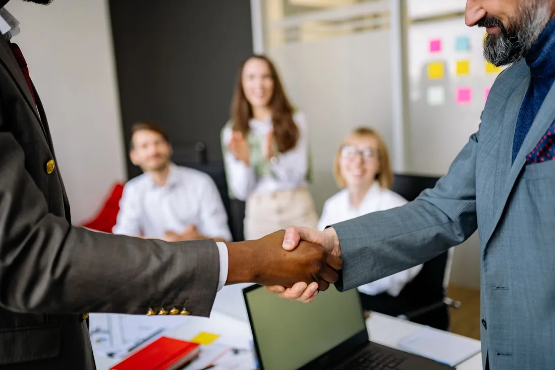Poignee de main entre deux dirigeants d'entreprise validant un accord de reservation groupee, equipe en arriere-plan