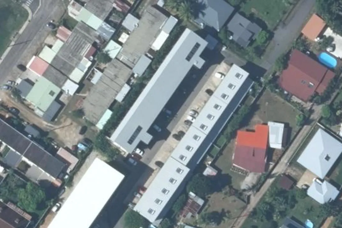 Vue aérienne verticale de la résidence Athelia à Cayenne : un long bâtiment à toiture grise et, en vis-à-vis, une rangée de logements accolés à toiture blanche, séparés par une allée de desserte bordée de voitures en stationnement