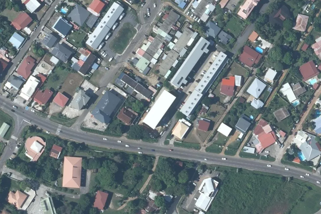 Vue aérienne de la route de Montabo (RD1) à Cayenne : la route traverse toute l'image, avec un carrefour et un passage piéton sur la gauche ; les deux bâtiments de la résidence Athelia occupent le quart supérieur droit