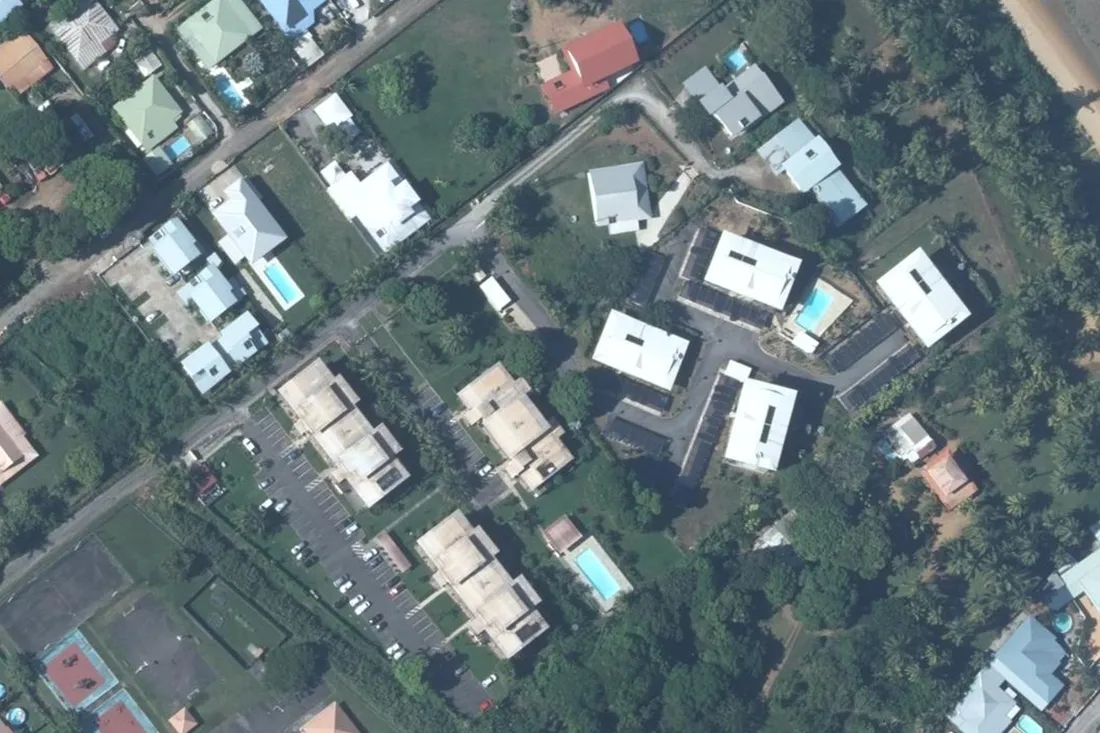 Vue aérienne de la rue Canne à Sucre à Montabo, Cayenne : la résidence Coconut Plage aux toitures blanches en haut à droite, la résidence Anse de Montabo aux toitures claires et son parking en bas à gauche