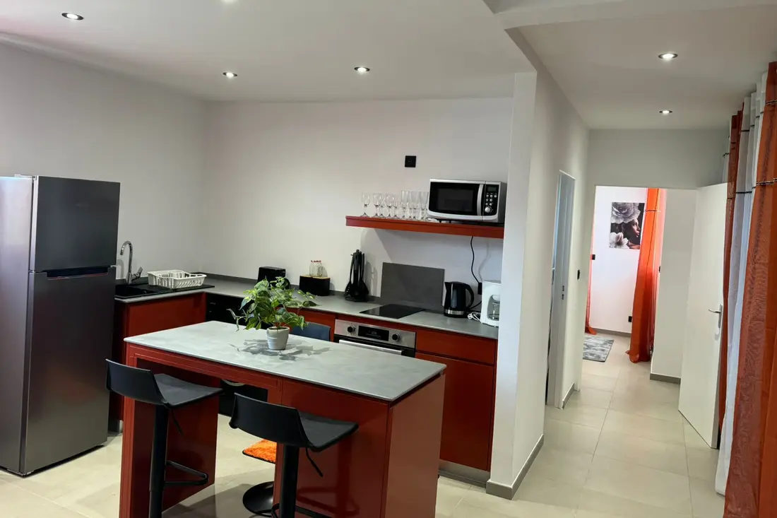 Cuisine d’un appartement de la Résidence Francis : îlot central rouge avec tabourets, four, micro-ondes et réfrigérateur