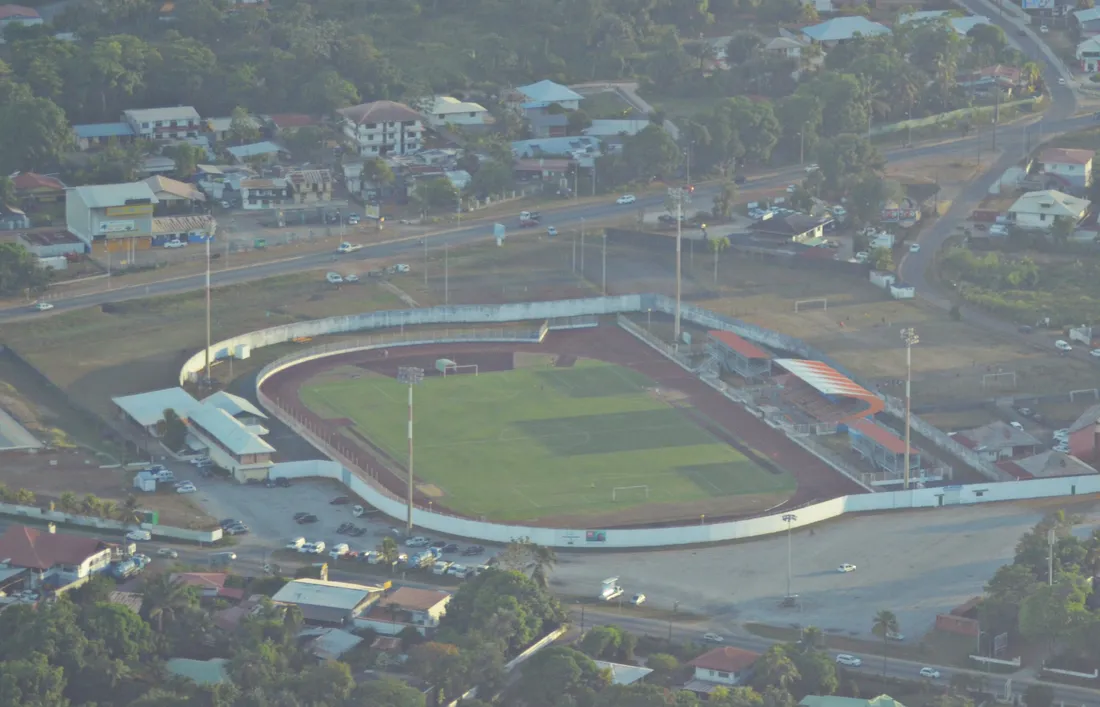 Vue aérienne oblique du stade Georges-Chaumet de Baduel à Cayenne, en Guyane, entouré de maisons, de commerces et de la route de Baduel