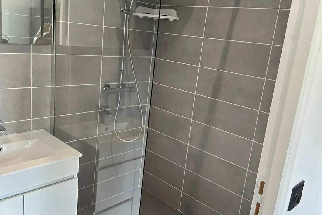 Douche à l’italienne d’un logement de la Résidence Francis : paroi vitrée, carrelage gris et colonne de douche