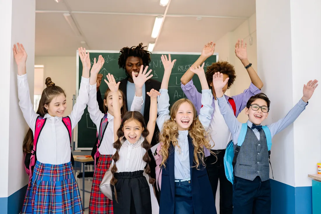 Enfants en uniforme scolaire levant les bras avec leur enseignant dans une salle de classe