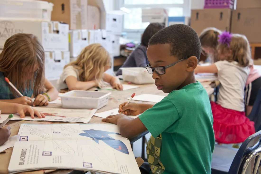 Écoliers concentrés autour d'une table dans une salle de classe, un garçon à lunettes dessinant pendant un atelier scolaire