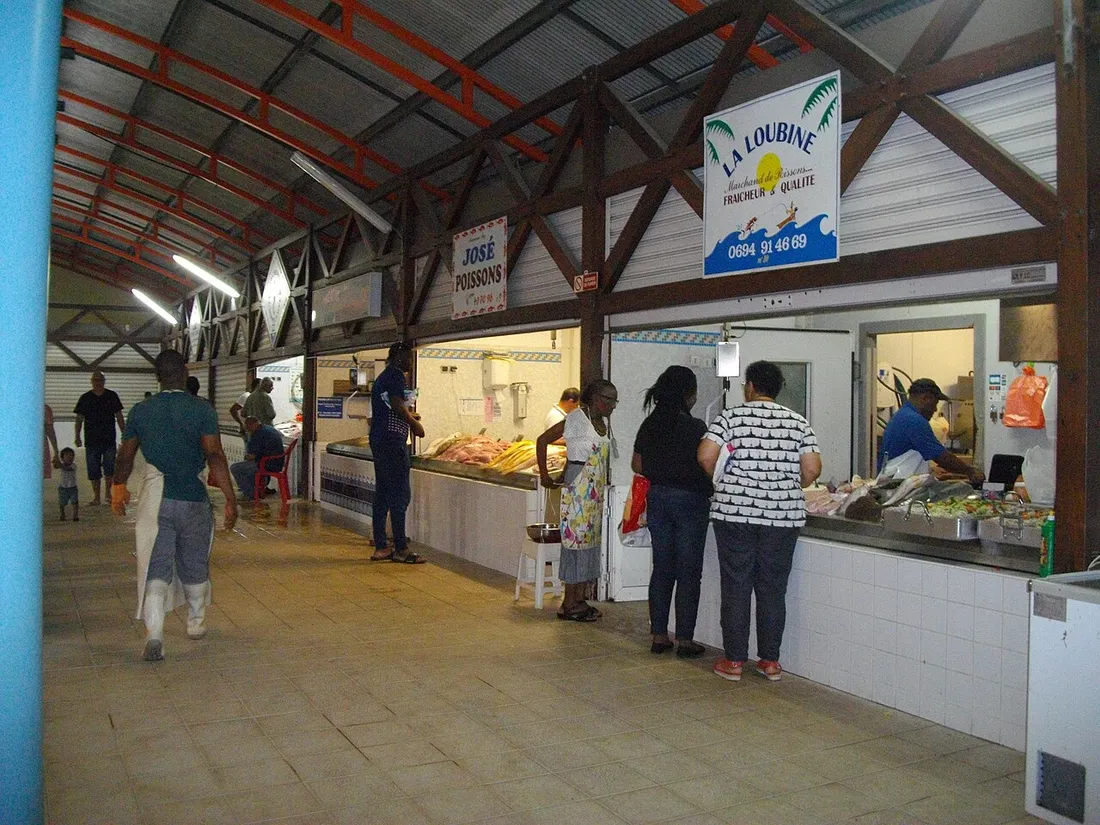 Halle couverte d'un marche de Guyane avec etals de poissons et clients faisant leurs courses sous la charpente metallique