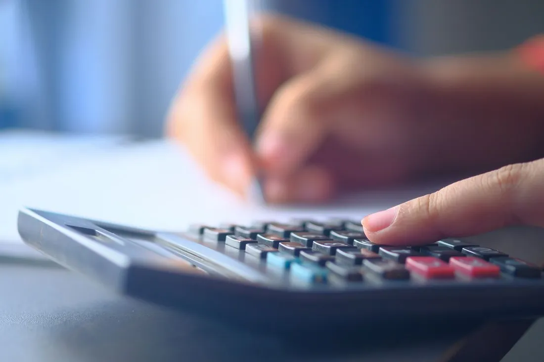 Main utilisant une calculatrice pour établir un budget, avec un stylo et des documents financiers