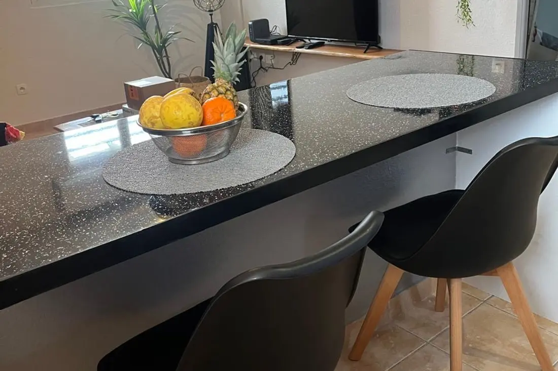 Breakfast bar in a Cayenne Chic apartment: speckled black counter, fruit bowl and two chairs facing the living area