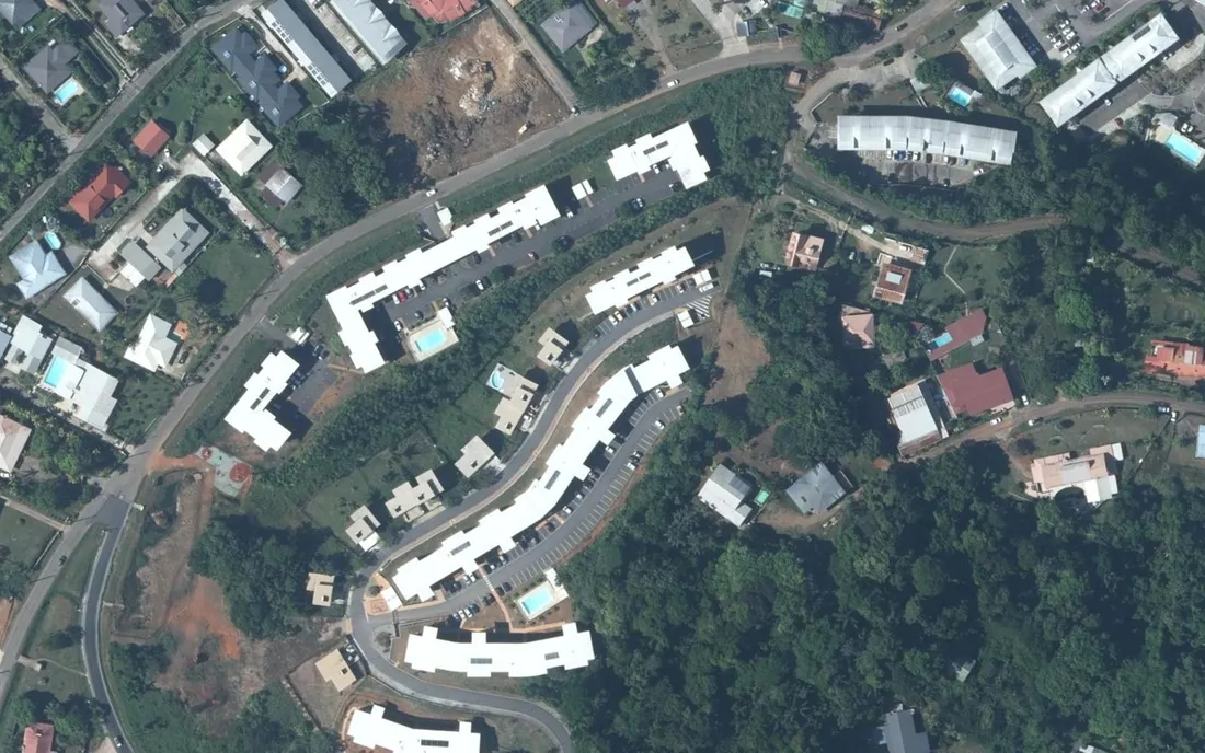 Vue aérienne verticale de petites résidences collectives récentes, avec parkings et piscines de copropriété, le long de la route de Suzini à Rémire-Montjoly (Guyane)
