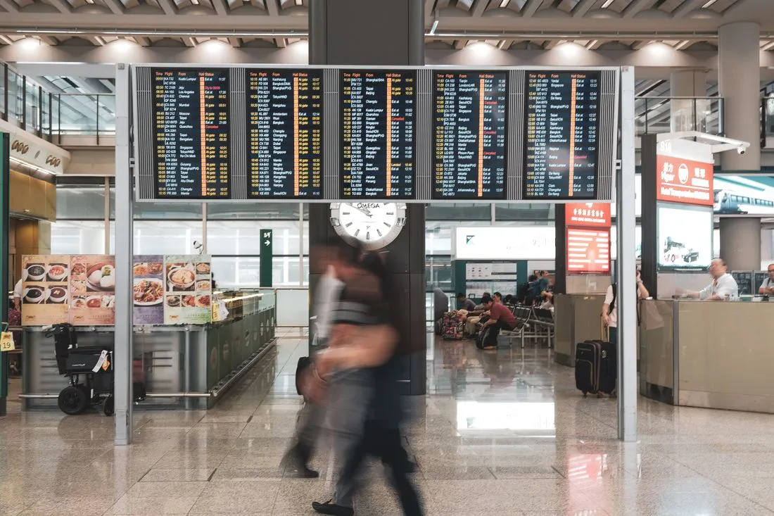 Tableau des departs d'un aeroport avec voyageurs et bagages dans le hall, illustrant les escales et horaires d'un vol Paris-Cayenne