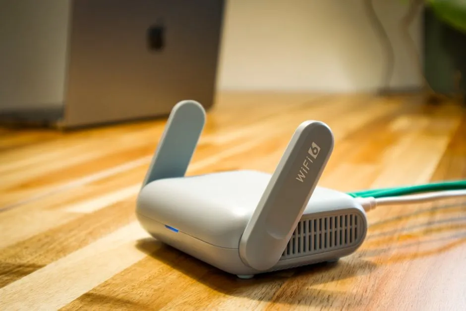 Routeur Wi-Fi 6 blanc à antennes posé sur un parquet, relié par un câble Ethernet, devant un ordinateur portable